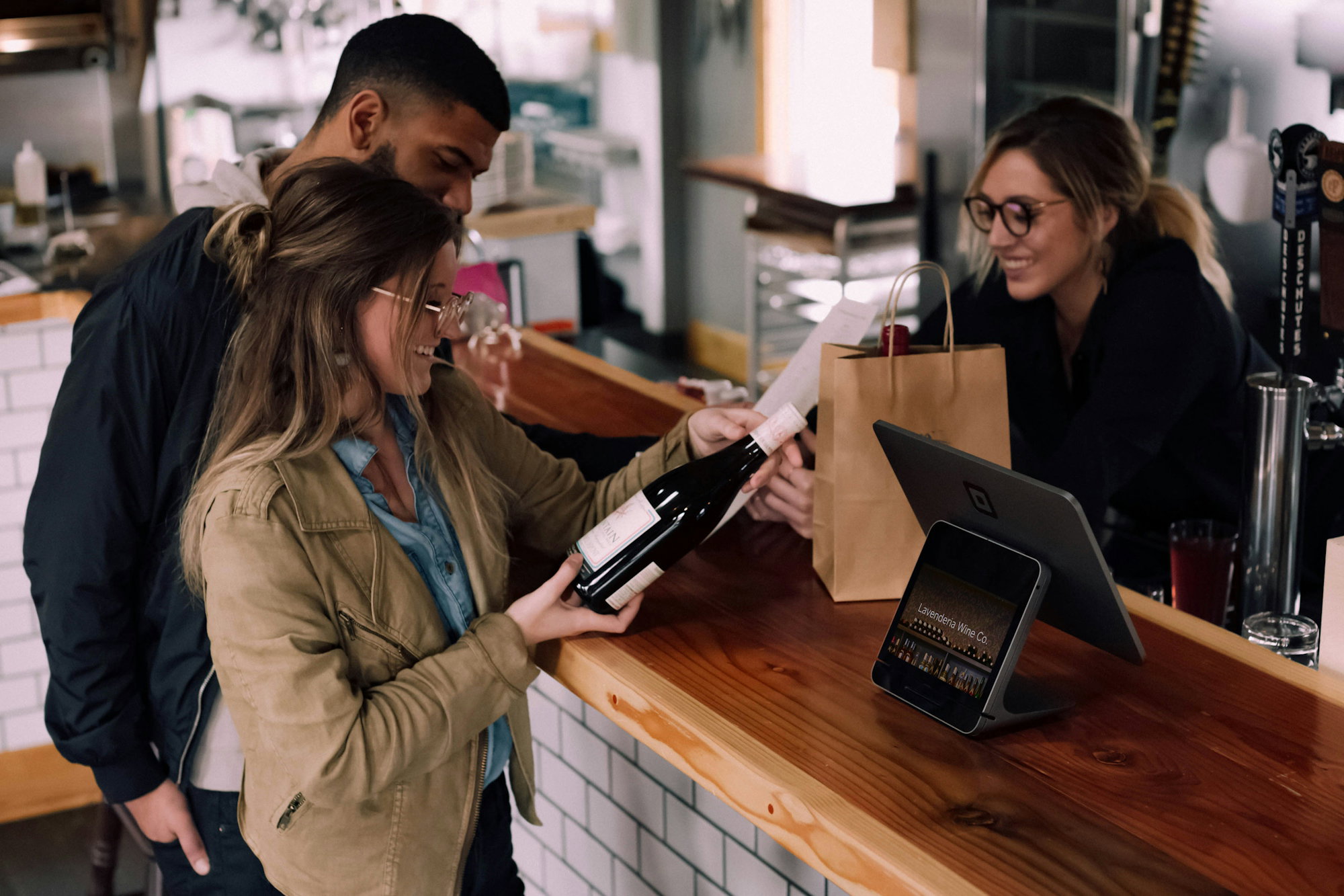 woman-holding-wine-bottle-beside-man-in-front-of-woman-smiling.jpg woman holding wine bottle beside man in front of woman smiling